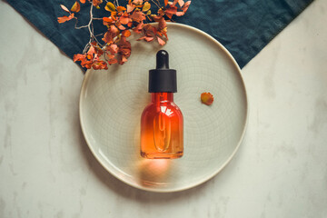 Natural cosmetics, serum in bottle with a pipette on a round dish. Spa and bio autumn skin care concept background