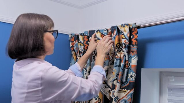 Woman hanging velvet curtains on metal hooks on cornice pipe