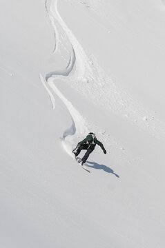 Active man riding snowboard down snowy mountain slope