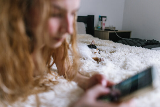 Blonde girl chatting and lying on bed with sleeping cat