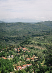 Top view of a European village in the green hills. Italian houses with red roofs, orchards in the valleys, and rich greenery.