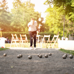 playing petanque guy through a ball above trees in city park outdoor activity sunshine	

