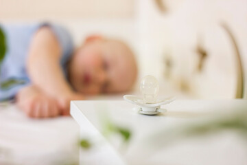 Fototapeta na wymiar Little baby boy is peacefully sleeping and a pacifier dummy liying on table near bed.