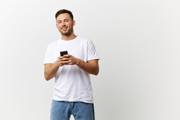 Cheerful tanned handsome man in basic t-shirt typing message with phone smile at camera posing isolated on over white studio background. Copy space Banner Mockup. Distance online communication concept