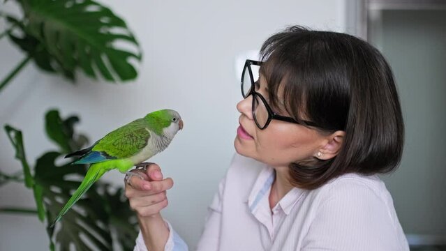 Mature woman at home with a pet parrot on her arm