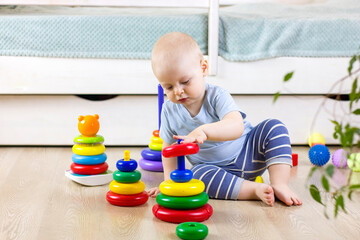 Cute baby boy toddler sitting on the floor at home and collects a pyramid toy.