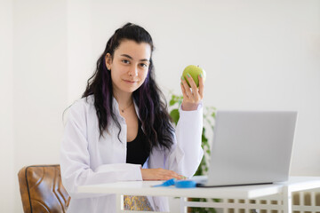 Dietitian doctor holding green apple in the hand sitting in her office at weightloss clinic.