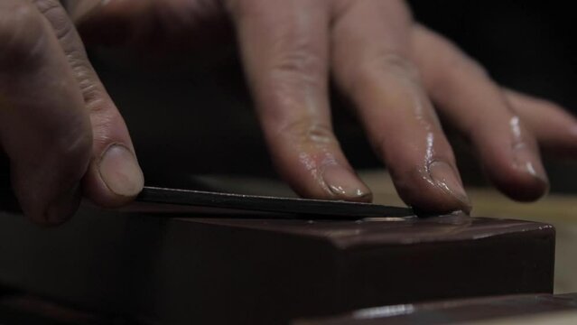 Master swordsmith is sharpening knife on grindstone with water