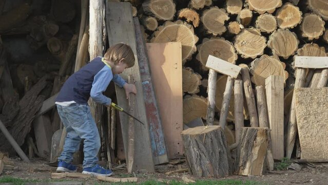 Little kid cutting the timber with hand saw in the wood workshop