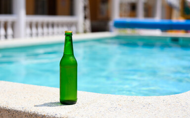 A bottle of cold beer by the pool in a hotel on a hot day. copyspace.
