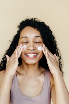 Cheerful female smearing cream on cheeks