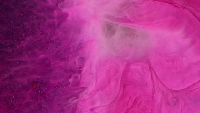 Abstract fantasy fluid art background. Swirling pink paint on a purple background. Macro video of pink smoke and clouds