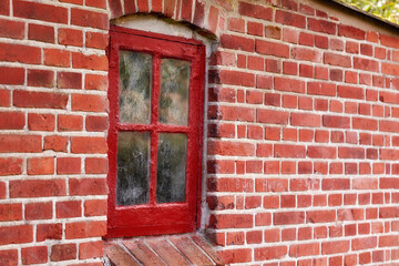 Old dirty window in a red brick house or home. Ancient casement with red wood frame on a historic building with clumpy paint texture. Exterior details of a windowsill in a traditional town or village