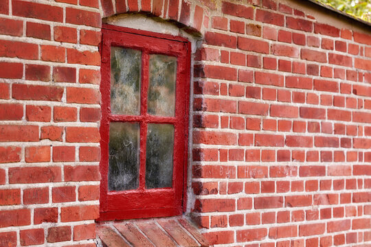 Old dirty window in a red brick house or home. Ancient casement with red wood frame on a historic building with clumpy paint texture. Exterior details of a windowsill in a traditional town or village