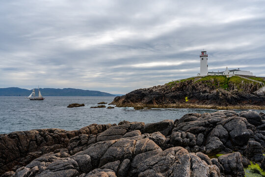 view of the Fanad Head Lighthouse on the northern coast of Ireland with an old two-masted sailboat sailing away