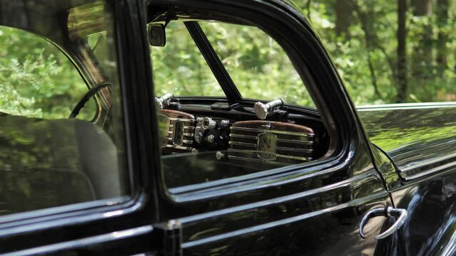 A close-up view of a black retro car in a summer green forest. Front view of the black retro car.