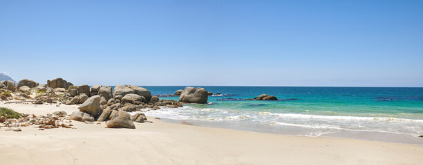Calm beach with white sand on a rocky natural seaside environment in a popular getaway location for a holiday in Cape town. Landscape of the ocean on a sunny day with blue sky and copy space
