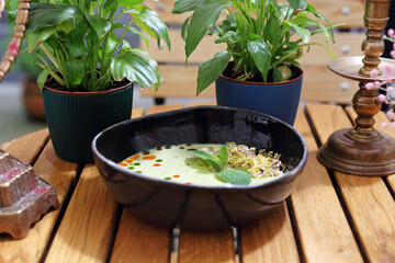 White vegetables cream soup in a modern black bowl, decorated with green leaves and colorful oil drops, selective focus.