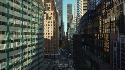 Forwards fly above street between modern high rise buildings with colour facades. Manhattan, New York City, USA