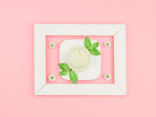 One scoop of vanilla ice cream in a square saucer with mint leaves and chamomile flowers in a white...
