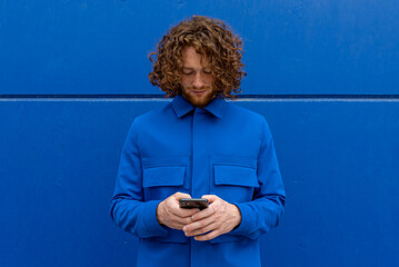 Redhead man using smartphone against blue wall
