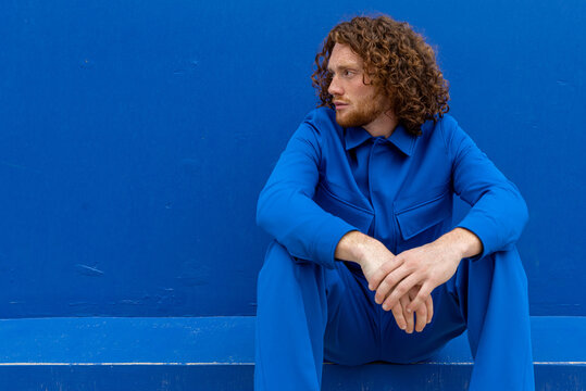 Redhead male sitting against blue wall