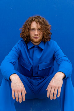 Redhead male sitting against blue wall