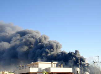 Fototapeta na wymiar Grande nuvola di fumo nero, incendio dietro edifici in città