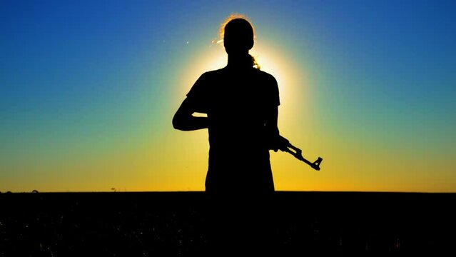 Ukraine War. A young man with a Kalashnikov assault rifle trains in the field. Silhouette of a man with a Kalashnikov assault rifle. The concept of war, terrorism, aggression against Ukraine.