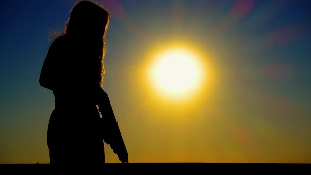 The problem of sexism. A young boy-girl with a Kalashnikov assault rifle at sunset. A transgender man with a Kalashnikov in a field at dawn. The concept of justice, equality, sexual minorities, LGBT.