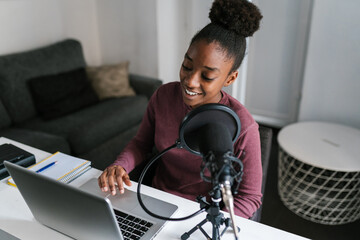 Joyful black woman using netbook and recording podcast