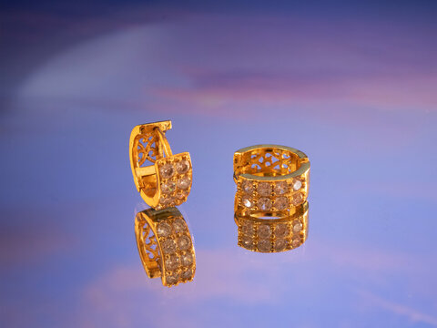 gold earrings with zirconias positioned on a purple glossy surface