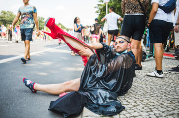 Man dramatically putting long red high heel boots on during Pride
