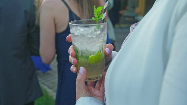 Caucasian Female Holding Glass of Refreshing Mojito Alcohol Drink Watching People Dancing on Wedding Reception Garden Party
