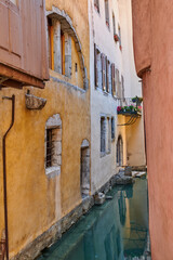 Fototapeta na wymiar Canal flowing between houses, roads and streets in the medieval part of the city of Annecy in France. Secluded and beautiful scenic view of a river running through a residential area in a small town