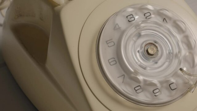 A mans hand removing the handset and rotating the dialer with his finger. Male finger dialing phone number on an old white rotary telephone with disc dial. Retro plastic phone. Close up.