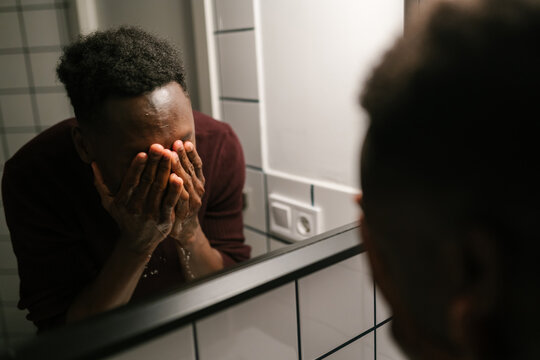 Black man washing face near mirror