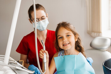 Cheerful girl child holding dental drill and smiling in dentistry. The child smiles at the consultation with the dentist.
