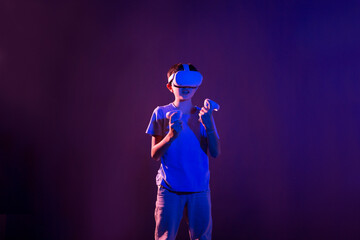 Video Gaming Concept. teenager boy playing with virtual reality goggles, VR headset, modern technology glasses  with neon light  on a colored background