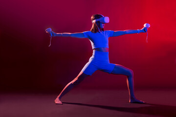 Fototapeta na wymiar woman practices yoga in VR headset, modern technology glasses with neon light on a colored background