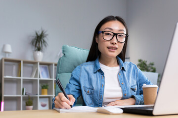 Job interview. A young beautiful Asian business woman in glasses sits at a desk, conducts an interview in the office, hires, writes down a questionnaire in a notebook, interviews the interlocutor