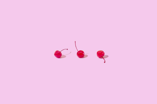 Three red maraschino cocktail cherry on pink background