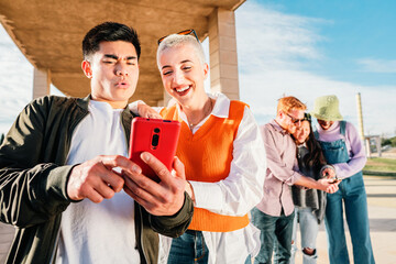 Two friends watching a video in a mobile phone. In the back three friends more browsing with a smartphone.