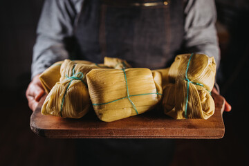 woman's hands holding chilean homemade humitas. Ground corn mix wrapped in corn husks and boiled