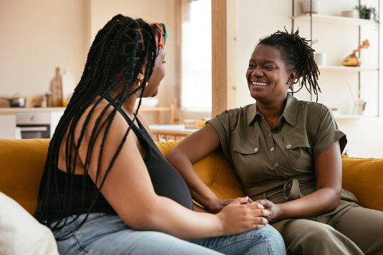 Black mother and daughter talking on sofa