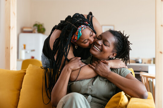 Black daughter kissing gleeful mom on cheek
