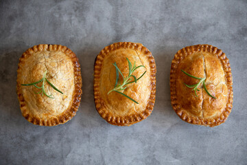 Three mini savory pies with thyme on dark grey background, top view