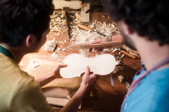 Unrecognisable violin luthiers comparing pieces
