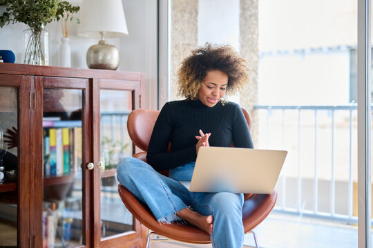 Smiling woman with laptop in chair in morning.