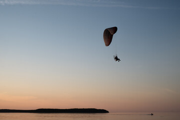 Paraglider pilot flies in the sky during sunset on beautiful beach. Paraplane silhouette. Adventure vacation and travel concept.